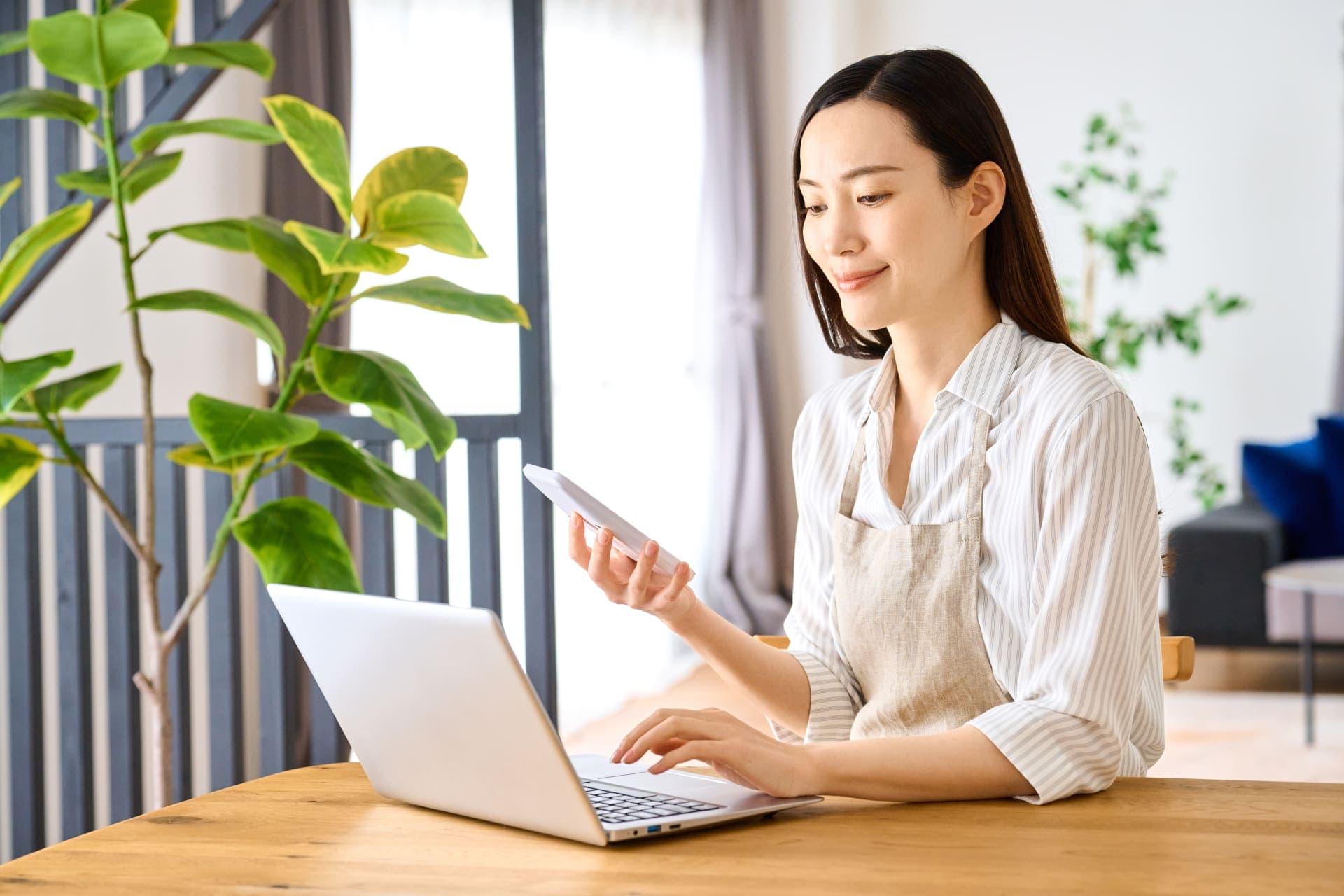 ノートパソコンとスマートフォンで作業する女性